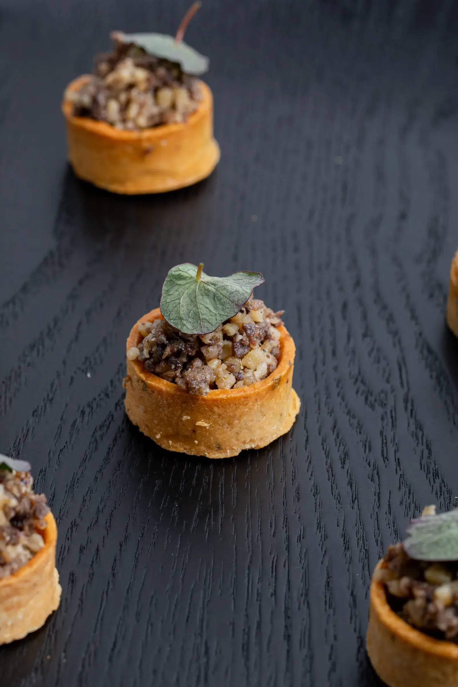 Small savoury tarts arranged on a dark surface