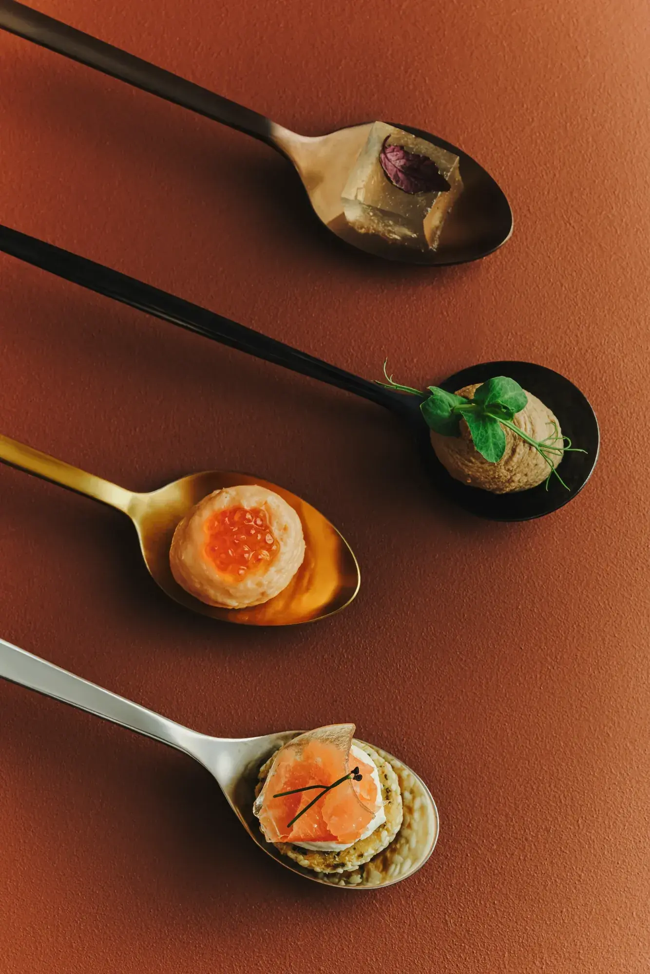 Small bites on serving spoons against terracotta