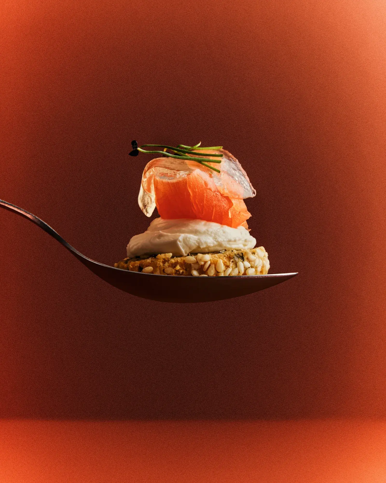 A salmon bite on a serving spoon against terracotta