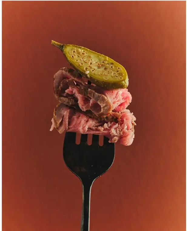 Slices of beef with a caper berry on a fork