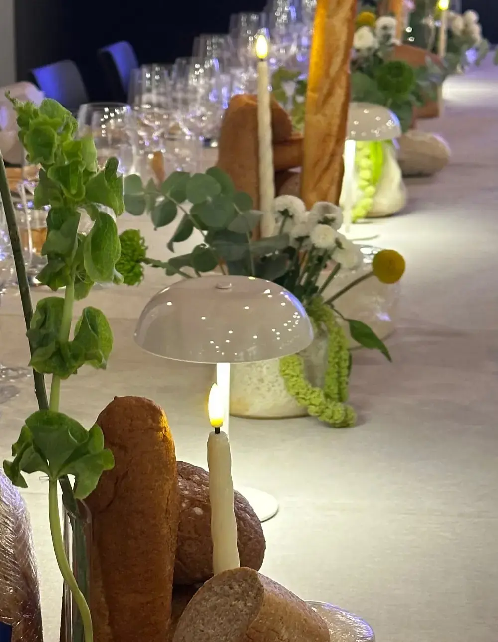 Table detail with bread, candles, a table lamp and flowers along a long table