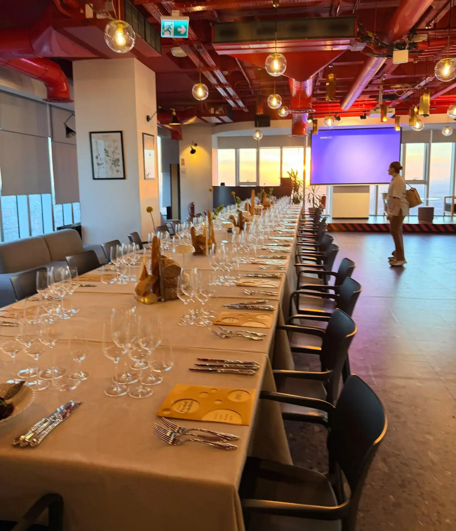A long dinner table set with glassware and bread arrangements at sunset