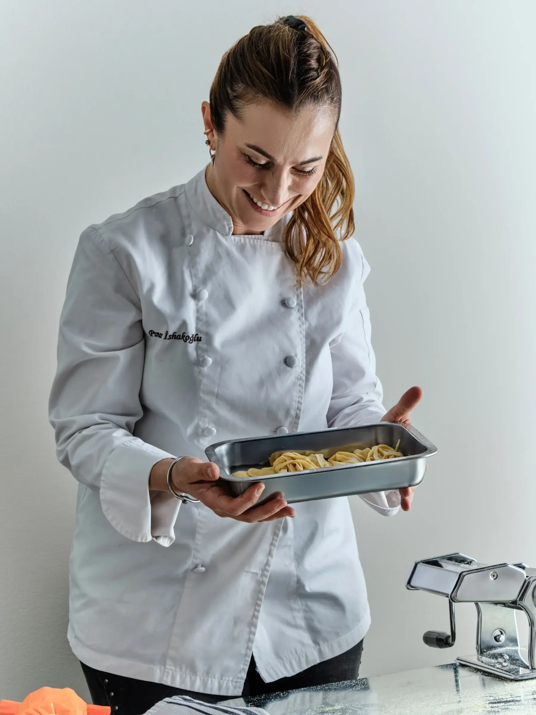 Pınar İshakoğlu smiling as she holds a tray of fresh handmade pasta